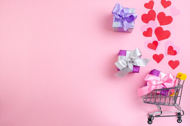 top view small gifts mini market trolley red hearts on pink background with copy place