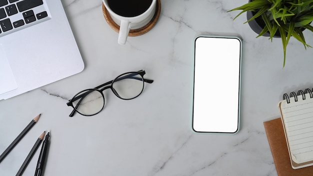 Top view smart phone with empty screen, glasses, coffee cup and laptop computer on marble background.