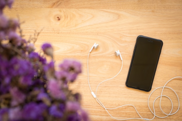 Top view of smartphone with dried flower and earphones on wood background. Copy space for 