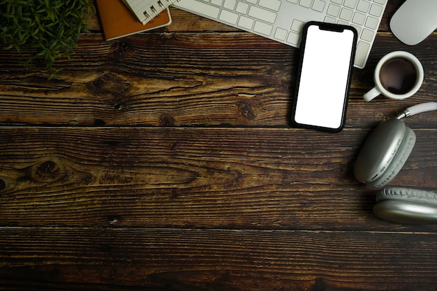 Top view of smartphone with empty screen headphone coffee cup and keyboard on wooden working desk Copy space for text