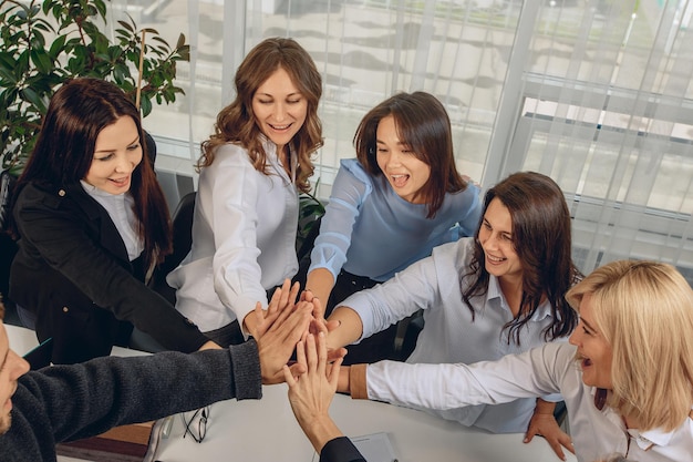 Top view of smiling cheerful team of office workers holding hands as a sign of support and leadership relationship. Job success concept