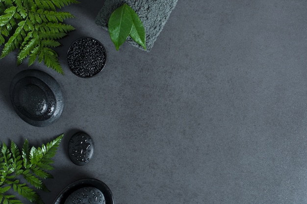 Top view of spa setting with hot stones and green ferns on gray background with copy sapce.