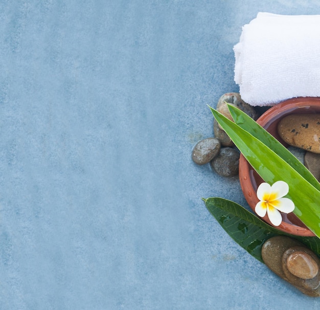 Top view of spa tropical flower and stones for massage therapy on blue background