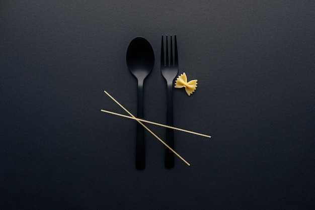 top view of spaghetti noodles on plastic cutlery near farfalle pasta on black background