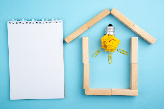 top view spiral notepad crumpled paper with idea light bulb concept in house shaped wood blocks on blue background