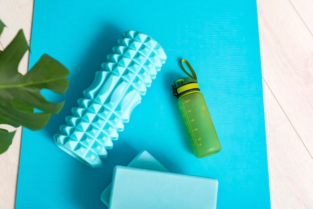 Photo top view of sports equipment on the yoga mat top view massage roller yoga bricks and bottle of water