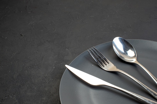 Top view of stainless cutlery set on a black plate on the left side on dark color background