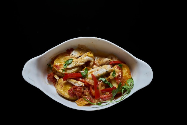 Top view of stewed chicken with vegetables in a white oval plate on black background