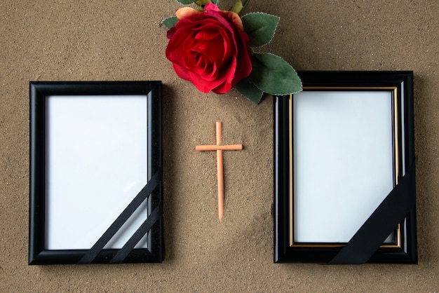 Top view of stick cross with red flower and picture frames on the sand