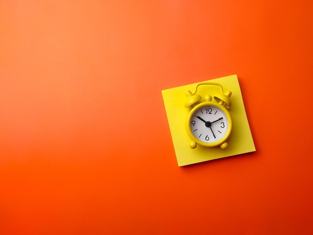 Photo top view sticky note and alarm clock on a orange background