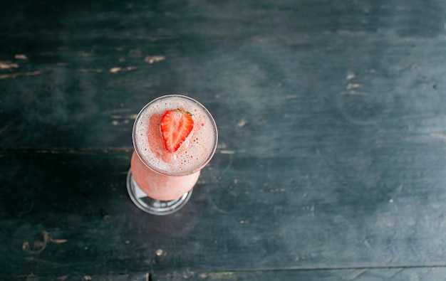 Top view of strawberry smoothie on dark wooden table View of strawberry milkshake on dark wood View from above of delicious strawberry smoothie with a strawberry on top on wood