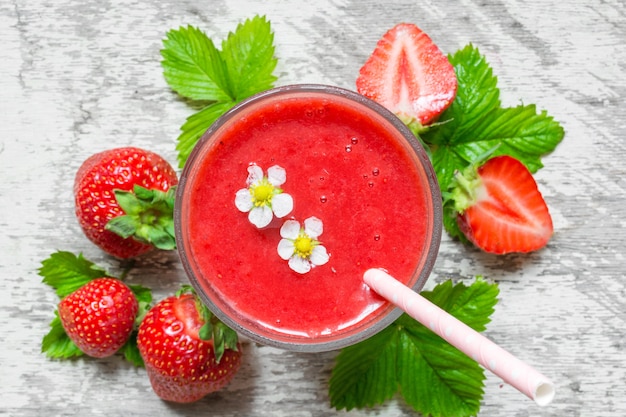 Top view of strawberry smoothie in a glass with straw, flowers and fresh berries