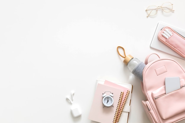 Top view stylish female backpack full of stationery supplies isolated. Back to school concept