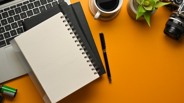 Top view of stylish workspace with notebooks, pen, laptop, camera, coffee cup and plant pot on yellow table