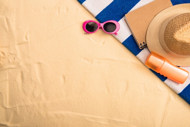 Top view of summer accessories and sunscreen on striped towel on sand