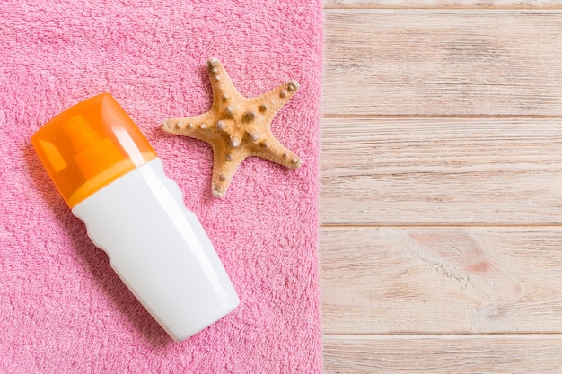 Photo top view of summer beach staff with copy space. seashells or seastar, a bottle of suncream and pink towel on wooden background. summer vacation concept.