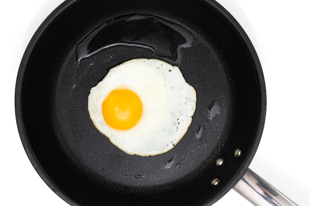 Top view of a sunny side up fried egg on a black pan isolated on a white background