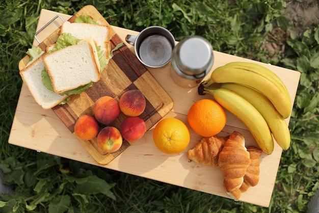 Top view of table with food in the open air thermos fresh bananas peaches oranges and sandwiches on the table in a tourist camp