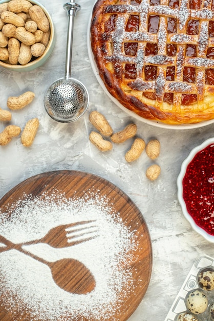 Top view tart with jam on plate other stuffs in bowls imprint fork and spoon made of flour on table