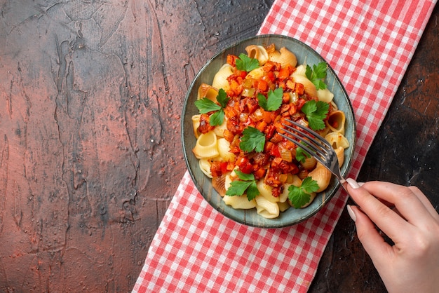 top view tasty pasta with tomato sauce in bowl fork in female hand on wooden table with copy place