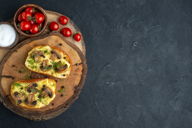 Top view of tasty snack with mushrooms tomatoes salt on wooden board on the right side on black background