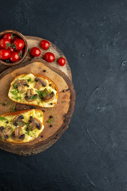 Top view of tasty snack with mushrooms tomatoes on wooden board on black background