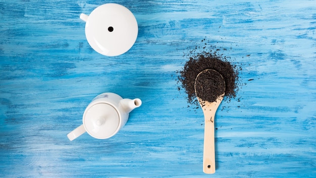 Top view on tea cup, tea leaves in wooden spoon on vintage blue background