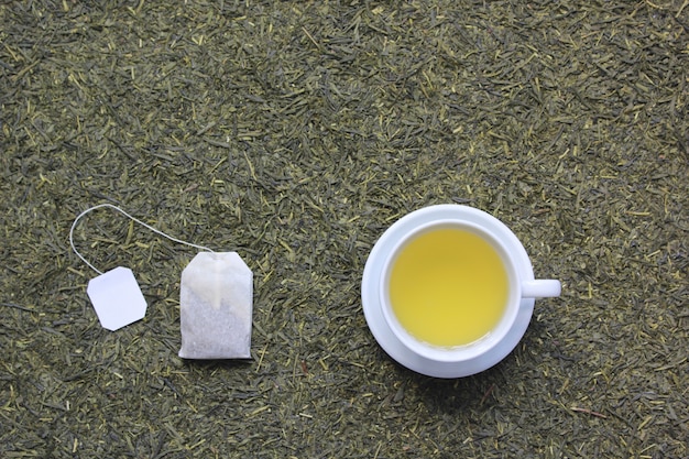 Photo top view of tea cup with tea bag on dried tea leaves background