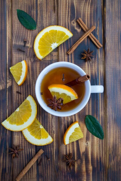 Top view of tea with orange, cinnamon and anise in the white cup on the wooden  background. Close-up.