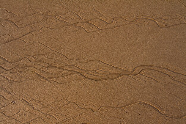 Top view of textured lines background on sand in the beach created by the low tide.