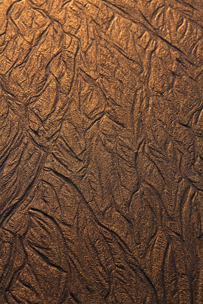 Top view of textured lines background on sand in the beach created by the low tide.