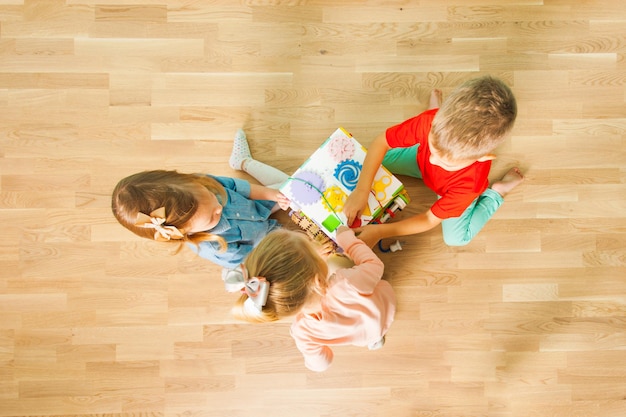 Photo top view of three adorable children playing with busy board on a wooden floor at home. company of small kids learning to play together. teamwork concept