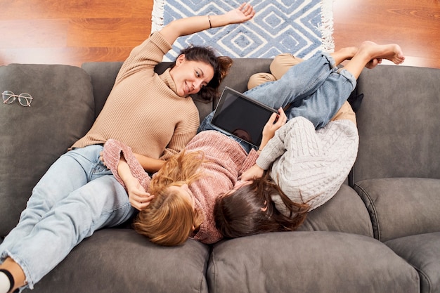 Top view of three female friends on the couch at home looking at a tablet