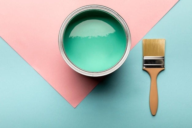 Top view of tin with green paint and brush on blue and pink surface