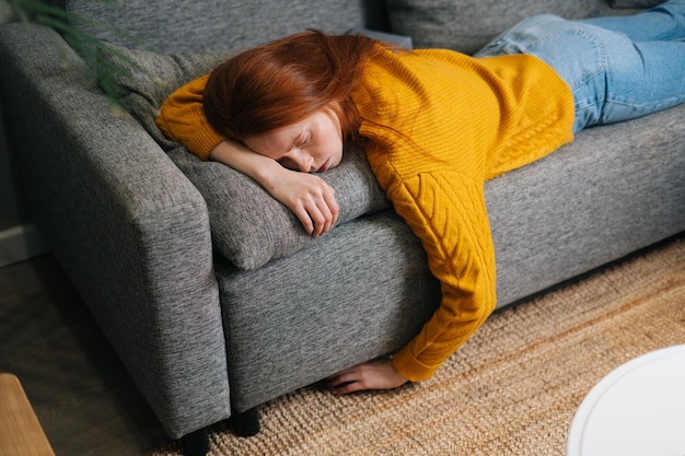 Top view of tired peaceful beautiful woman sleeping on cozy couch in living room lying on stomach Exhausted young female with closed eyes resting on sofa