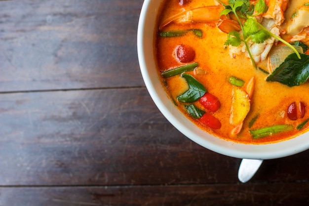 Top view Tom Yam kung Spicy Thai soup with shrimp in white bowl on wood table..