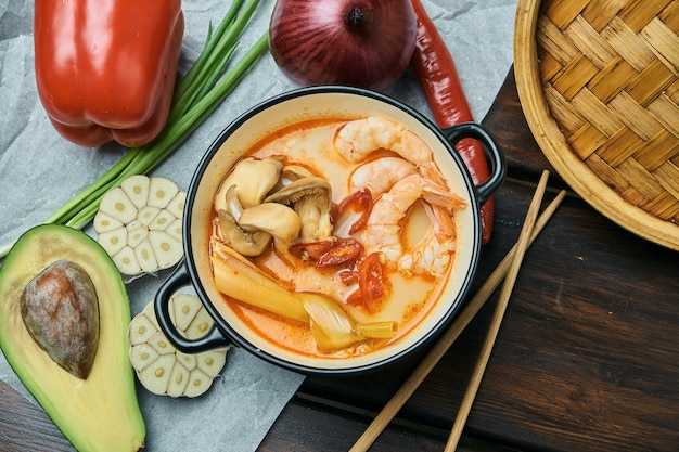 Top view tom yam with shrimp, seafood, coconut milk and chili pepper in composition with ingridients. Popular hot and sour Thai soup. Copy space. Tom yum