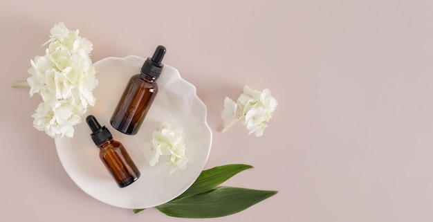 Top view of two cosmetic bottles with a dropper with a natural product for additional selfcare on a white abstract plate banner