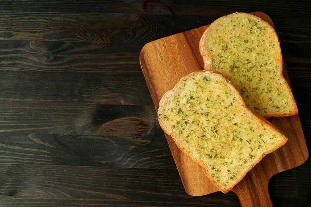 Top View of Two Delicious Homemade Garlic Butter Toasts on Breadboard Served on Dark Brown Table