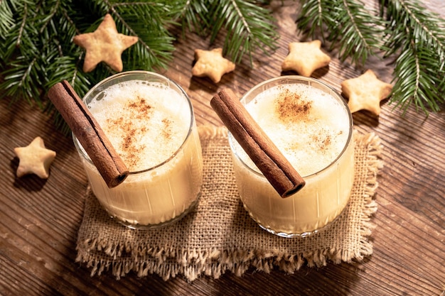 Top view to two glasses of Xmas eggnog with cinnamon fir branches cookies stars on wooden table