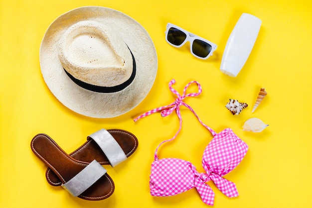 Top view of two pieces pink swimming suit and beach accessoties on yellow