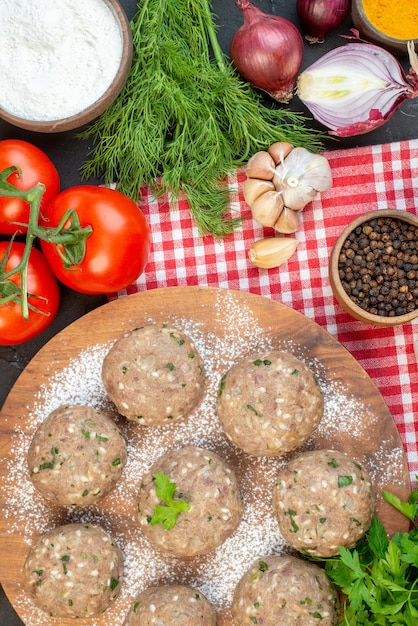 Top view of uncooked meat balls with green in a brown plate and fresh vegetables flour pepper green on red stripped towel on black background