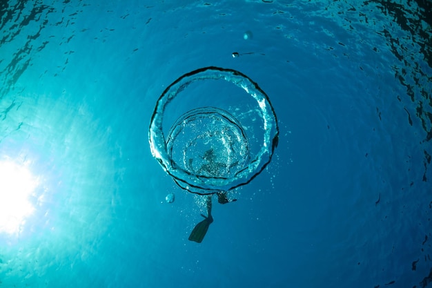 Top view of unrecognizable male tourist in flippers swimming under transparent blue water with bubbles on sunny day