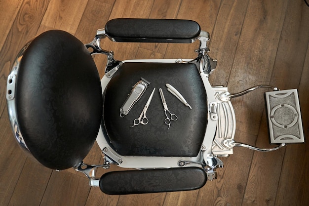 Top view of various barber tools on black leather chair on wooden floor in hairdressing salon