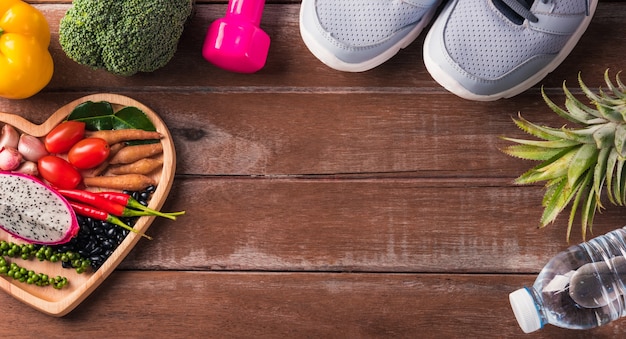 Top view of various fresh organic fruit and vegetable in heart plate and sports shoes