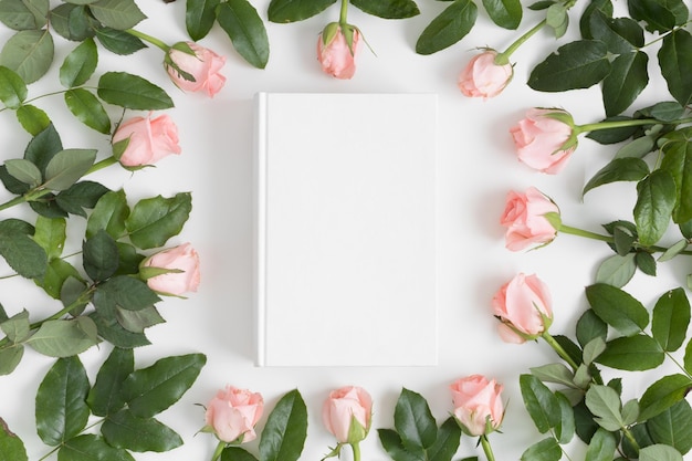 Top view of a white book mockup surrounded by pink roses on a white table