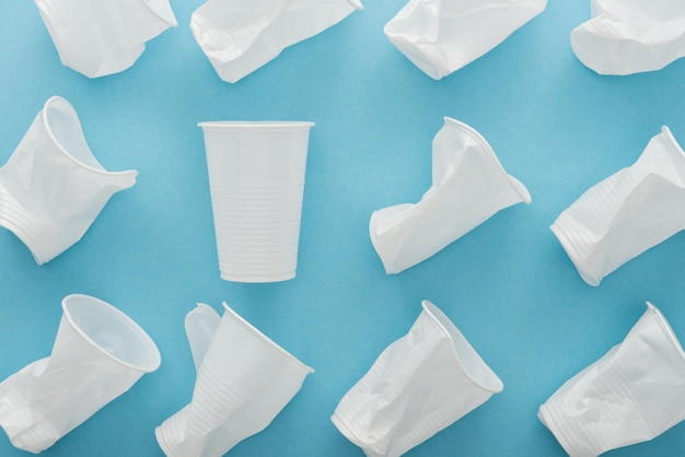 Top view of white and crumpled plastic cups on blue background