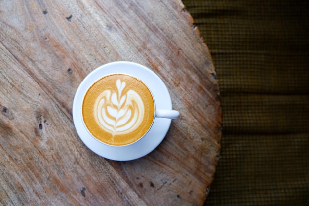 Top view of white cup of cappuccino with latte art on wooden table