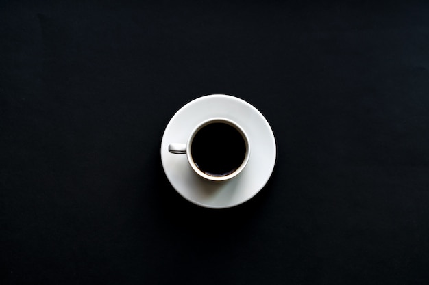 Top view of white cup of coffee on black background. Minimal flat lay. 