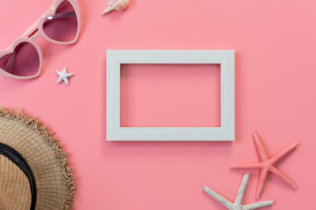 Top view of white frame, sunglasses, straw hat on pink c